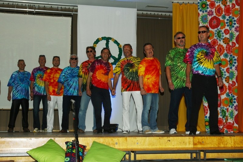 Die Mainfinken singen auf der Bühne in bunten Batik-T-Shirts vor einem Peace-Zeichen aus Blumen