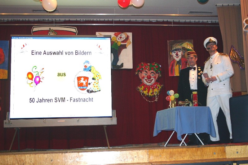 Zwei Männer in Fastnachtsuniformen auf der Bühne neben einer Leinwand mit dem Titel „Eine Auswahl von Bildern aus 50 Jahren SVM-Fastnacht“