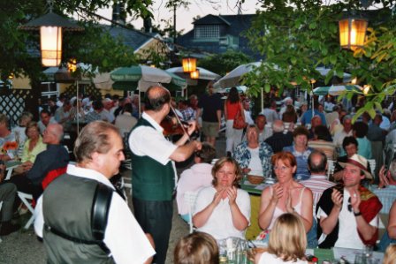 Abendstimmung im Gastgarten eines Wiener Heurigen: ein Geiger spielt zwischen den voll besetzten Tischen, die Gäste klatschen mit
