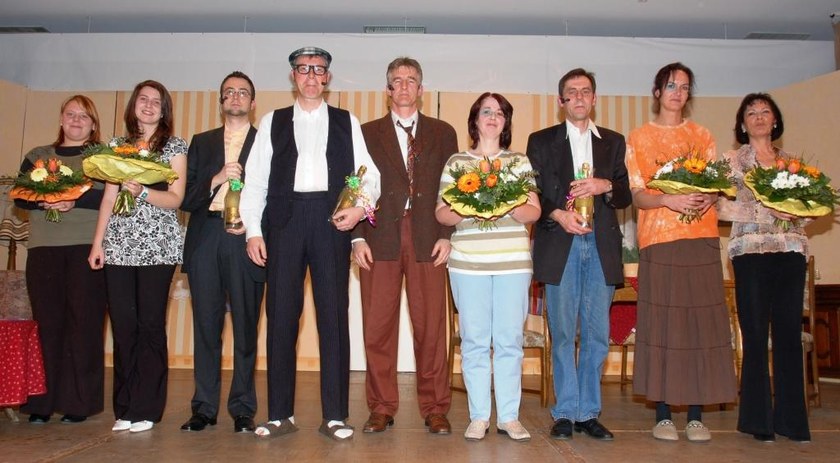 Die neun Darsteller der SVM-Theatergruppe mit Blumensträußen und Sektflaschen auf der Bühne des Bürgerhauses