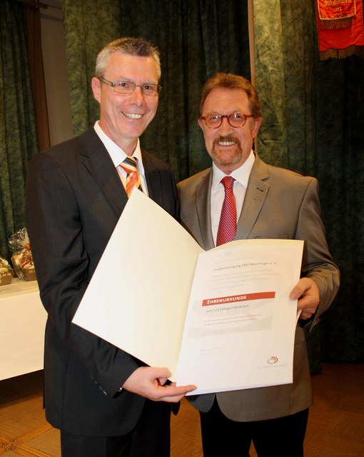 Zwei Männer präsentieren lächelnd die aufgeschlagene Ehrenurkunde des Deutschen Chorverbands zum 125-jährigen Bestehen