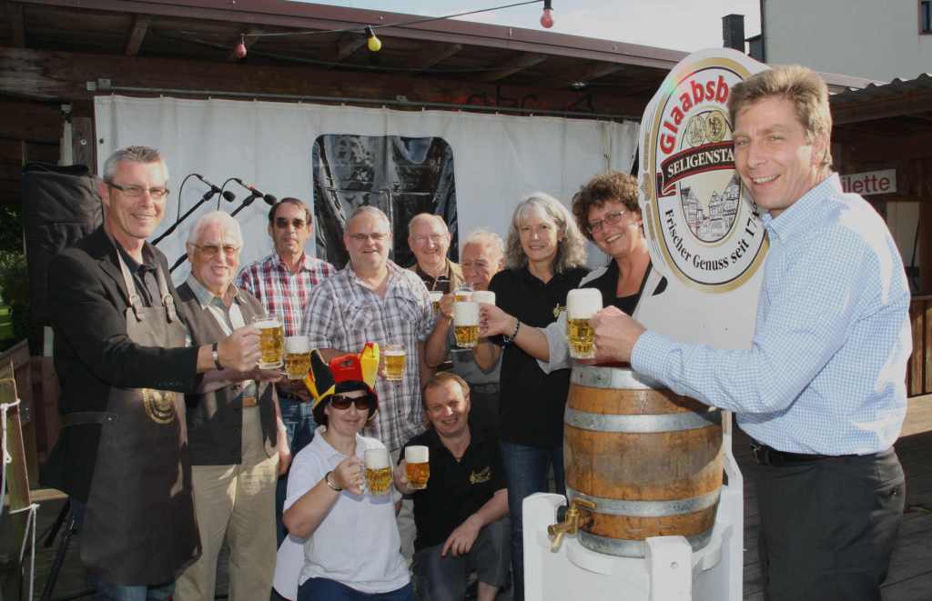 Beim Bieranstich prostet eine Gruppe Vereinsmitglieder mit gefüllten Biergläsern am Holzfass der Seligenstädter Glaabsbräu