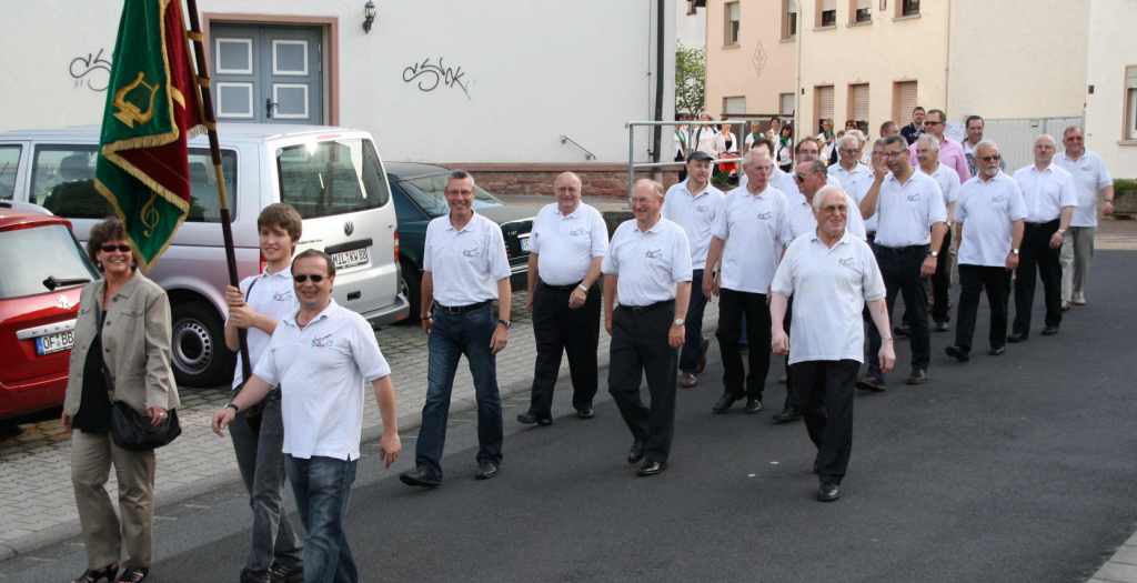Die Männer der SVM in weißen Polohemden beim Sternmarsch durch die Ortsstraßen, vorneweg die grün-rote Vereinsfahne