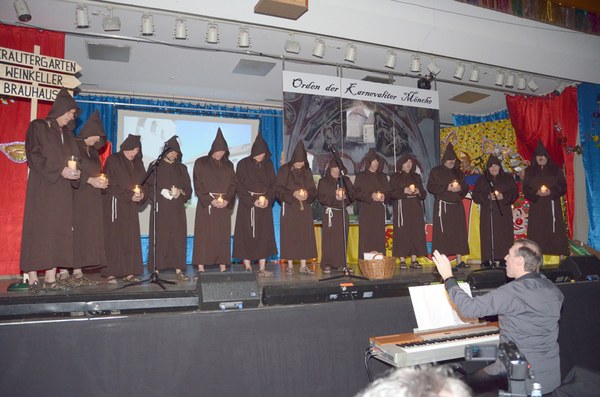 Die Mainfinken als Mönche in braunen Kutten mit Kerzen unter dem Banner „Orden der Karnevaliter Mönche“, davor der Chorleiter am Keyboard