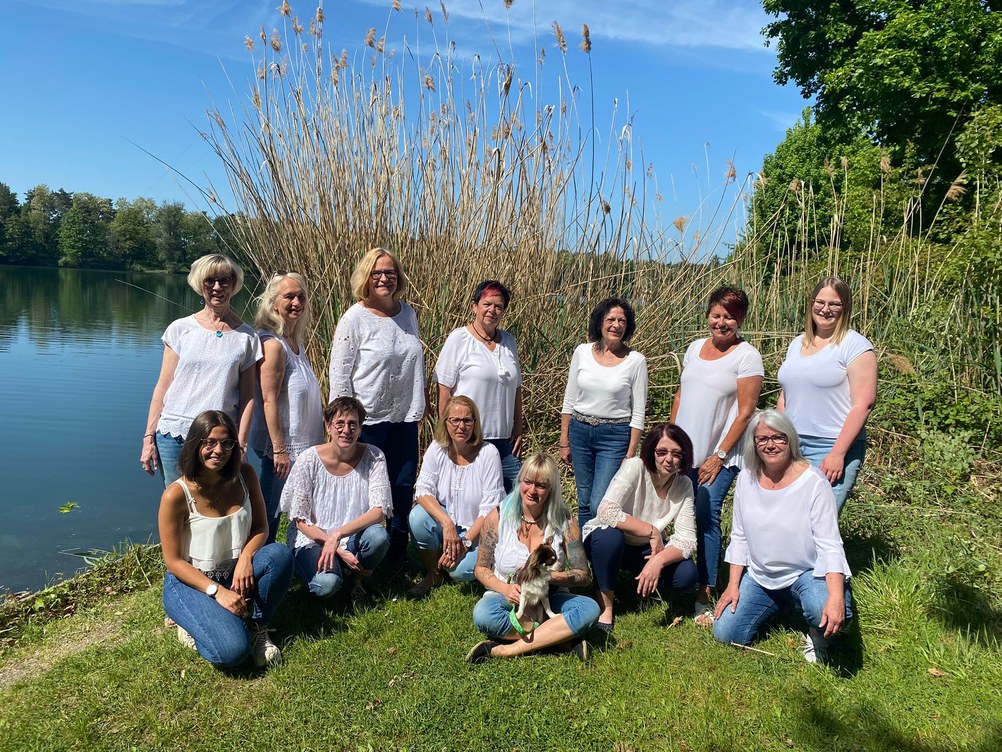 Die Moafährladies in weißen Oberteilen und Jeans vor dem Schilf am Ufer des Anglersees, vorne in der Mitte eine Sängerin mit kleinem Hund