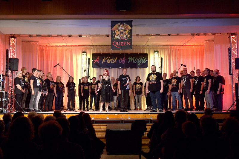 Der Chor Crescendo in Queen-T-Shirts auf der Bühne des Bürgerhauses, davor die Solisten, darüber das Banner „A Kind of Magic“